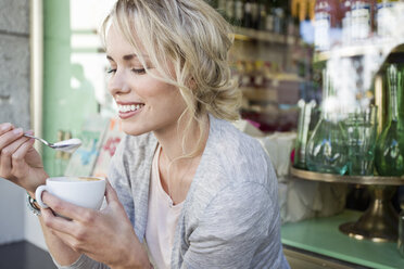 Mittlere erwachsene Frau isst Schaum aus einer Kaffeetasse in einem Straßencafé - CUF04172