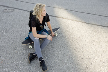 Female skateboarder sitting on skateboard - CUF04176