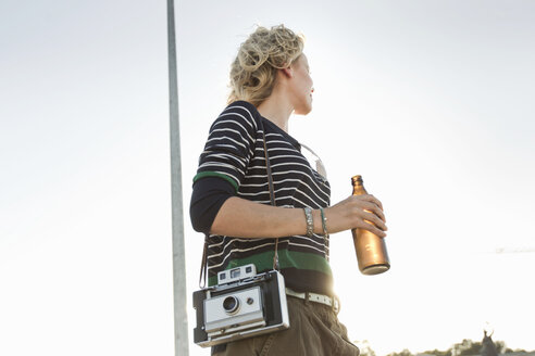 Mid adult woman carrying beer bottle and vintage camera in park - CUF04220