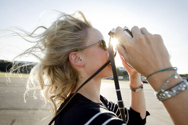 Mittlere erwachsene Frau mit fliegendem Haar, die mit einer alten Kamera fotografiert - CUF04225