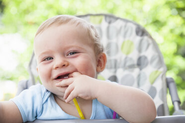 Porträt eines kleinen Jungen mit Fingern im Mund auf einem Hochstuhl im Garten - CUF04259
