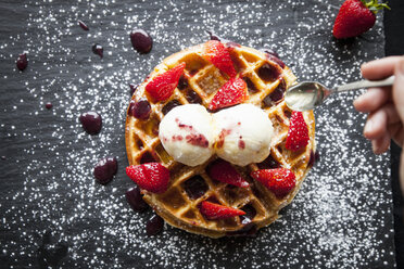 Weibliche Hand hält Löffel über Erdbeeren und Eiswaffel auf Schiefer - CUF04276