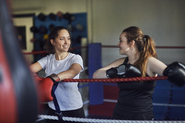 Young female boxers leaning against boxing ring ropes chatting - CUF04292