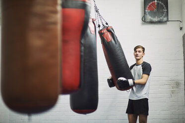 Junger männlicher Boxer hebt einen Sandsack im Fitnessstudio - CUF04300