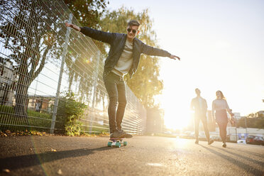Junger männlicher Skateboarder, der auf einer sonnenbeschienenen Straße Skateboard fährt - CUF04302