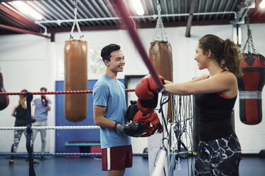 Female boxer leaning on boxing ring ropes talking to male boxer - CUF04306