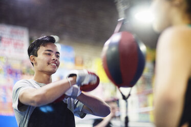 Junger männlicher Boxer, der im Fitnessstudio auf einen Sandsack einschlägt - CUF04320