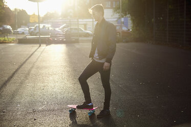 Junger männlicher Skateboarder mit Skateboard auf sonnenbeschienener Straße - CUF04321