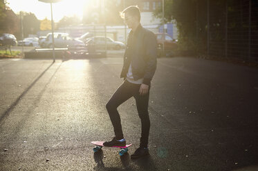 Young male skateboarder with skateboard on sunlit street - CUF04321