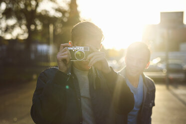 Junger Mann fotografiert mit seiner Kamera auf einer sonnenbeschienenen Straße - CUF04322