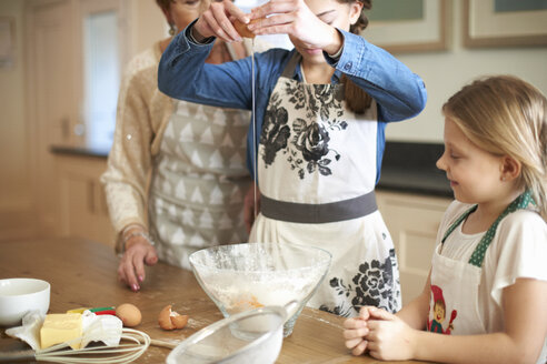 Ältere Frau und Enkelinnen schlagen Eier für Kekse auf - CUF04378