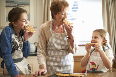 Ältere Frau und Enkelinnen essen frisch gebackene Weihnachtsbaumkekse - CUF04386