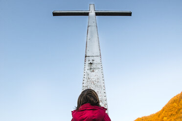 Rückansicht eines Jungen, der zu einem hoch aufragenden Kreuz und einem blauen Himmel blickt - CUF04393