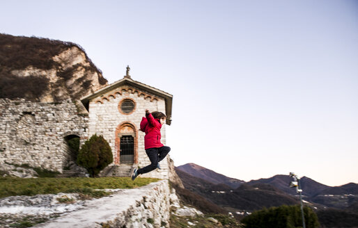 Junge springt von hoher Mauer in Berglandschaft, Italien - CUF04394