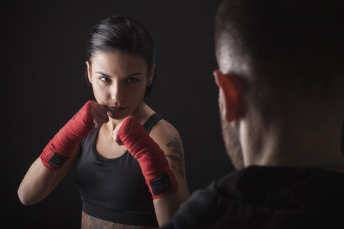 Porträt einer jungen Frau in Kampfhaltung, die einem Fitnesstrainer gegenübersteht - CUF04420