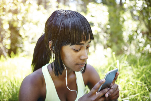 Junge Frau in ländlicher Umgebung, die ein Smartphone benutzt und Kopfhörer trägt - CUF04441
