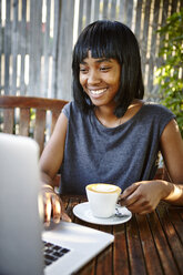 Young woman sitting outdoors, using laptop, drinking coffee - CUF04447