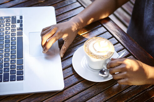 Junge Frau sitzt im Freien, benutzt einen Laptop, trinkt Kaffee, Mittelteil - CUF04448