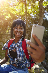 Junge Frau im Wald, die ein Smartphone benutzt und einen Videoanruf führt, Kapstadt, Südafrika - CUF04467