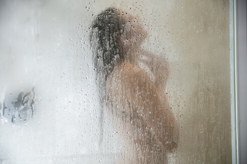 Young woman in shower behind steamed glass door - ISF00963