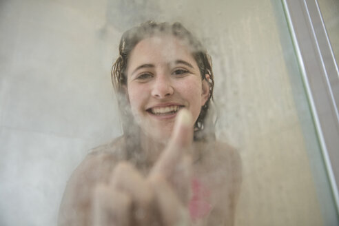 Porträt einer jungen Frau in der Dusche, die auf eine beschlagene Glastür zeichnet - ISF00965