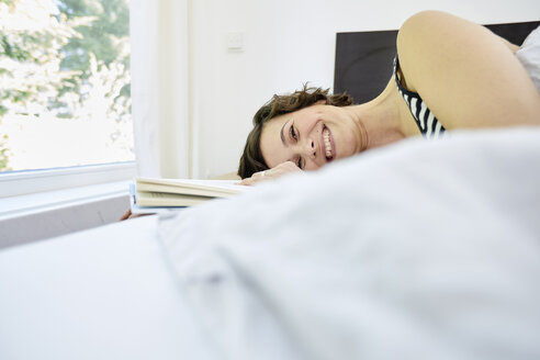 Mittlere erwachsene Frau, entspannt auf dem Bett, hält ein Buch, lächelt - ISF01018
