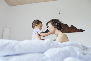 Mutter sitzt mit ihrem kleinen Mädchen im Bett, Gesicht zu Gesicht, nachdenklicher Ausdruck - ISF01020