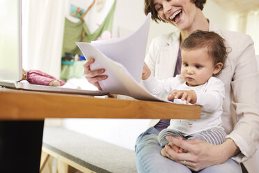 Mother looking at paperwork with baby girl sitting on her lap - ISF01035