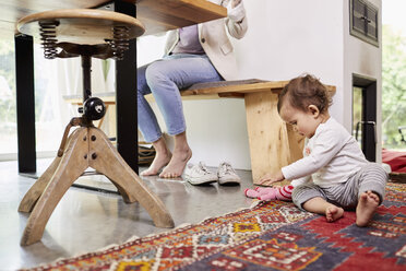 Mother working at kitchen table, whilst baby girl plays on floor. low section - ISF01036