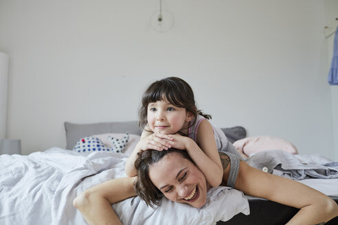 Mutter und Tochter liegen auf dem Bett, die Tochter liegt auf dem Rücken der Mutter - ISF01070