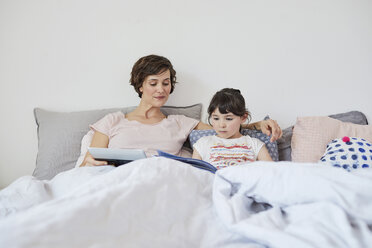 Mutter und Tochter entspannen sich im Bett, Tochter liest ein Buch, Mutter hält ein digitales Tablet - ISF01073