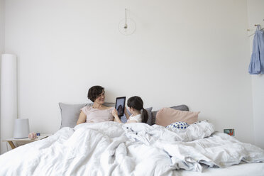 Mother and daughter relaxing in bed, daughter photographing mother using digital tablet - ISF01074