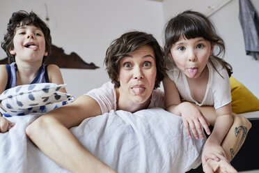Portrait of mother, son and daughter, lying on bed, poking tongue out - ISF01078