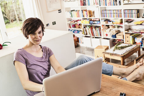 Mittlere erwachsene Frau zu Hause, sitzend am Tisch, mit Laptop - ISF01094