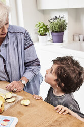 Großmutter und Enkel bereiten Essen in der Küche vor, Enkel mit fragendem Blick - ISF01100