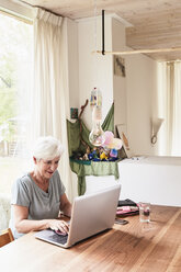 Ältere Frau sitzt am Tisch und benutzt einen Laptop - ISF01107