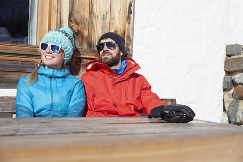 Ehepaar sonnt sich im Winter auf einer hölzernen Berghütte, lizenzfreies Stockfoto