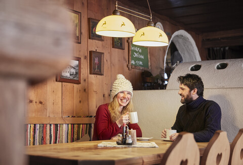 Glückliches Paar trinkt heißes Getränk in rustikaler Berghütte, lizenzfreies Stockfoto