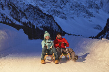 Glückliches Paar beim Schlittenfahren in einer schneebedeckten Landschaft bei Nacht - CVF00493