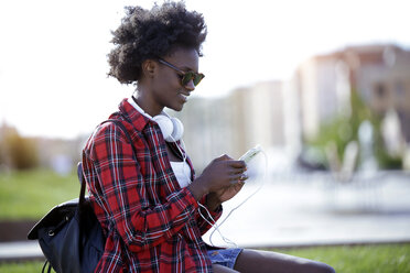 Smiling young woman with backpack and headphones using cell phone - JSRF00041