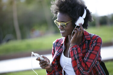 Porträt einer glücklichen jungen Frau, die mit Kopfhörern und Smartphone Musik hört - JSRF00045
