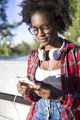 Porträt einer jungen Frau mit Kopfhörern, die ein Mobiltelefon benutzt - JSRF00046