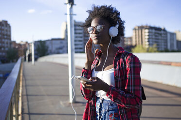 Portrait of young woman on a bridge listening music with headphones - JSRF00049