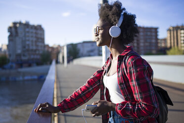 Junge Frau auf einer Brücke, die mit Kopfhörern Musik hört - JSRF00070