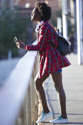 Young woman with backpack standing on a bridge listening looking at distance - JSRF00071