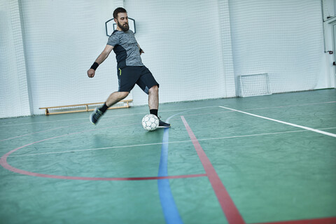 Mann spielt Hallenfußball und schießt den Ball, lizenzfreies Stockfoto