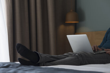Young man lying on bed using laptop, partial view - SKCF00452