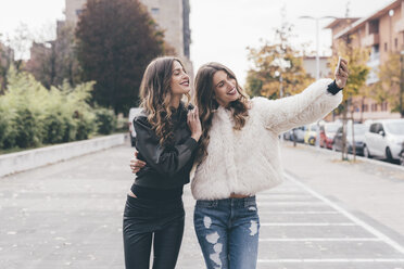 Zwillingsschwestern, die im Freien spazieren gehen und ein Selfie mit ihrem Smartphone machen - CUF04503