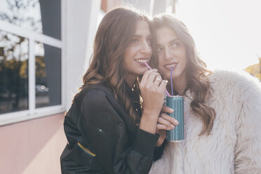 Twin sisters, outdoors, drinking can of soft drink with straws - CUF04525