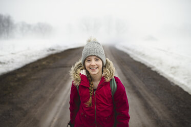 Portrait of girl in knit hat standing in middle of dirt road in fog - CUF04540